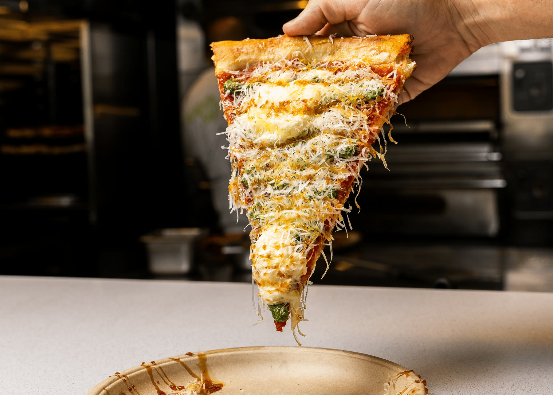 Porción de pizza de Kalis sostenida frente al horno